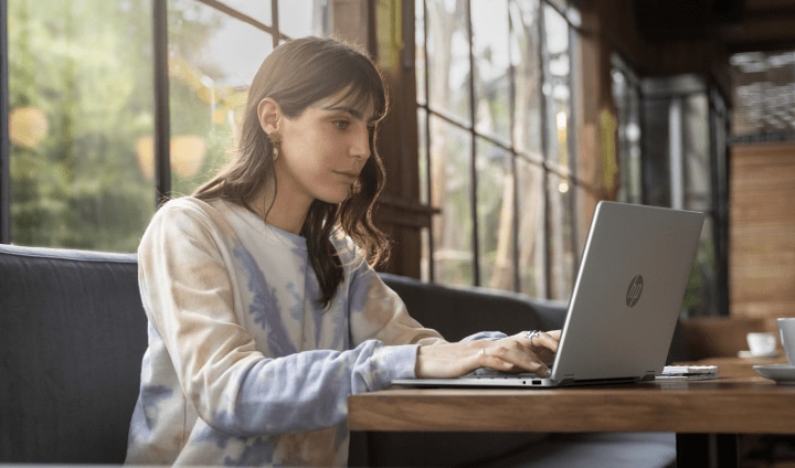 A person sitting at a table in a café using their HP OmniBook 5 laptop