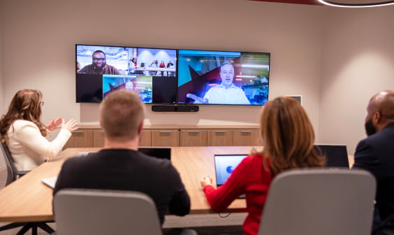 professionals at a conference table facing a large screen conference call display with video call in progress