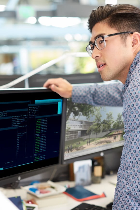 IT professional administrator standing, in his work cubicle are two HP monitors
