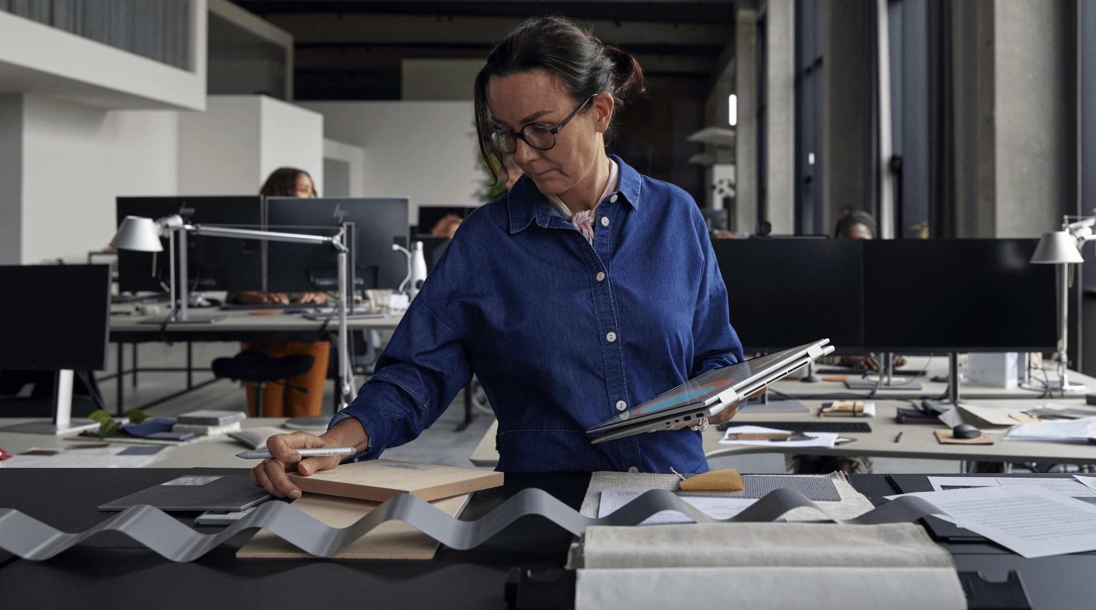 Woman standing at worktable with textiles, wood, and metal samples, working on an HP laptop