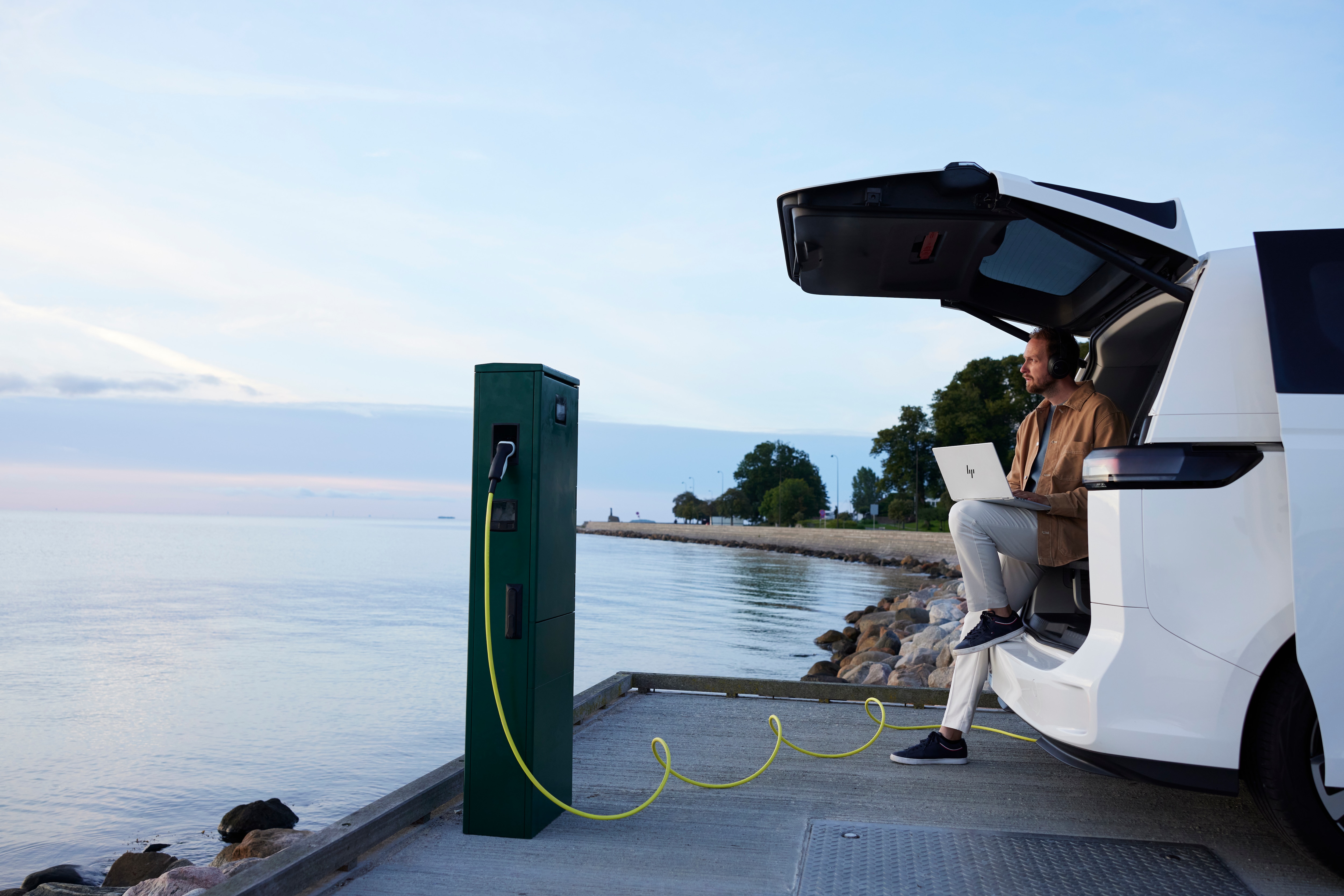 A man using an HP laptop while sits on his electric van waiting for it to charge