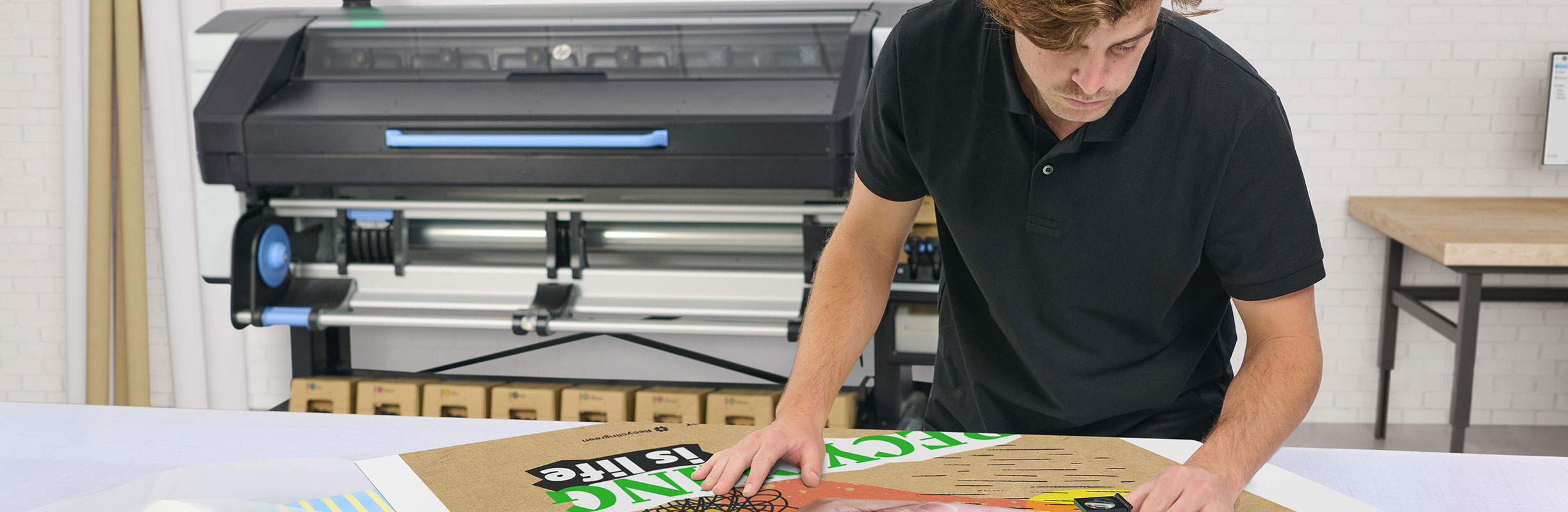 Person checking printed media on a desk in front of an HP Latex printer