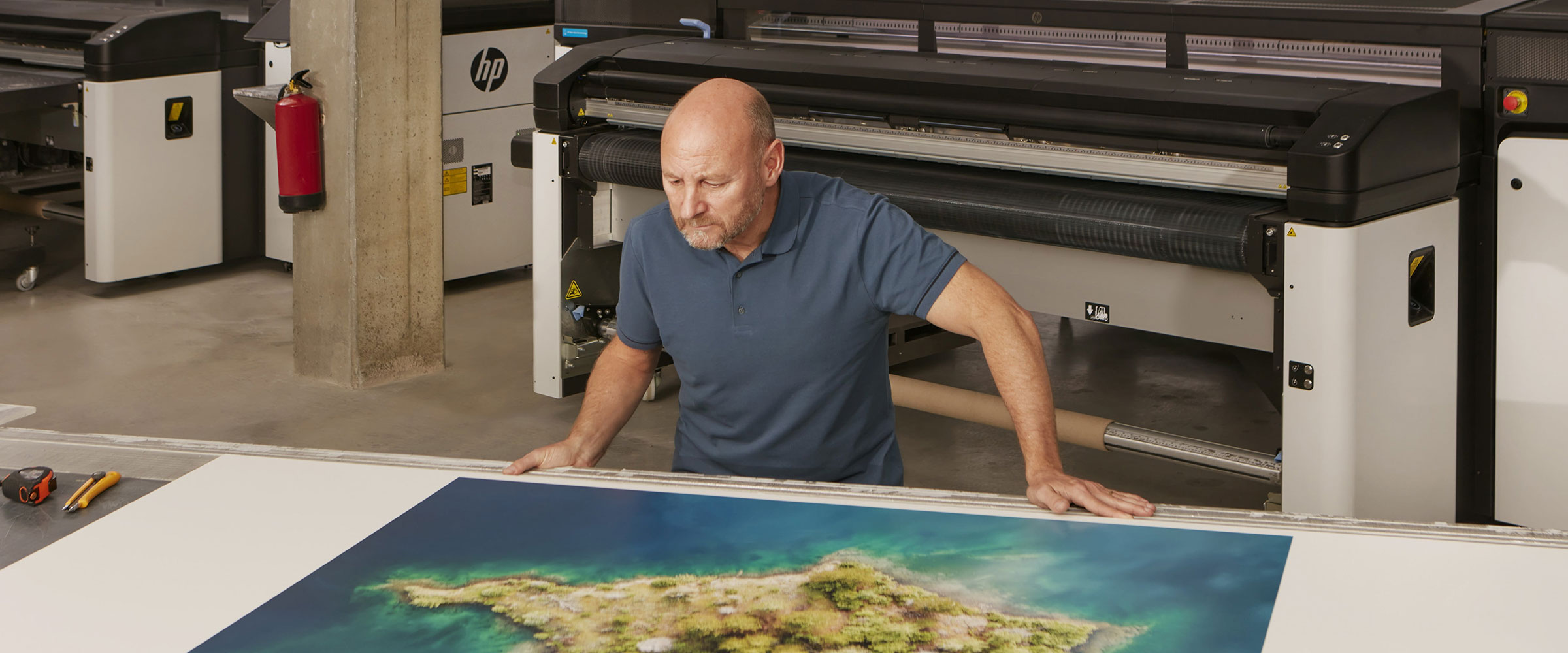 Person checking printed media over a work table in front of an HP Latex R2000 Plus printer
