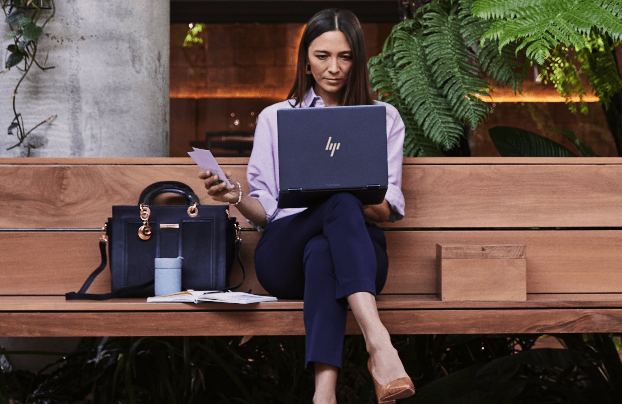 A woman using an HP laptop on her lap while sitting on a wooden garden bench.