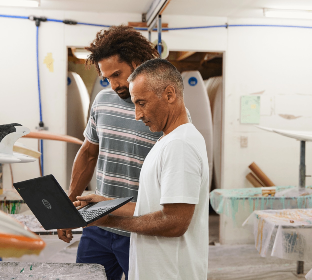 Men collaborate on laptop while making surfboards