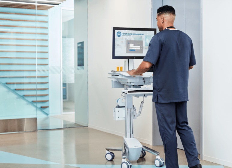 A male nurse pushing a medical cart that has an HP Engage system.