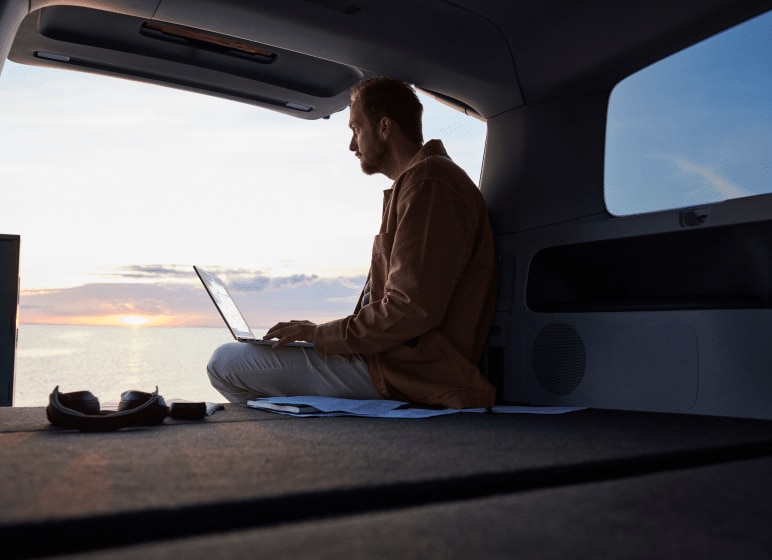 A digital nomad man using an HP laptop inside his camper parked near the coast.