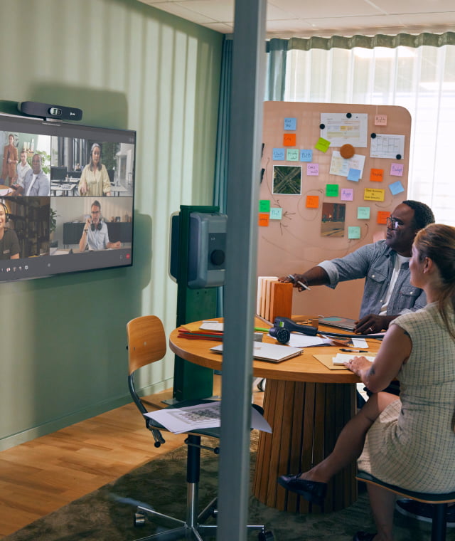 Team collaborating in small meeting room with colleagues on video call