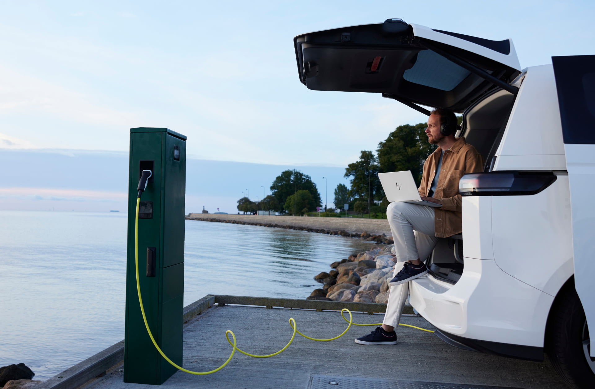Man working on laptop from EV at beach