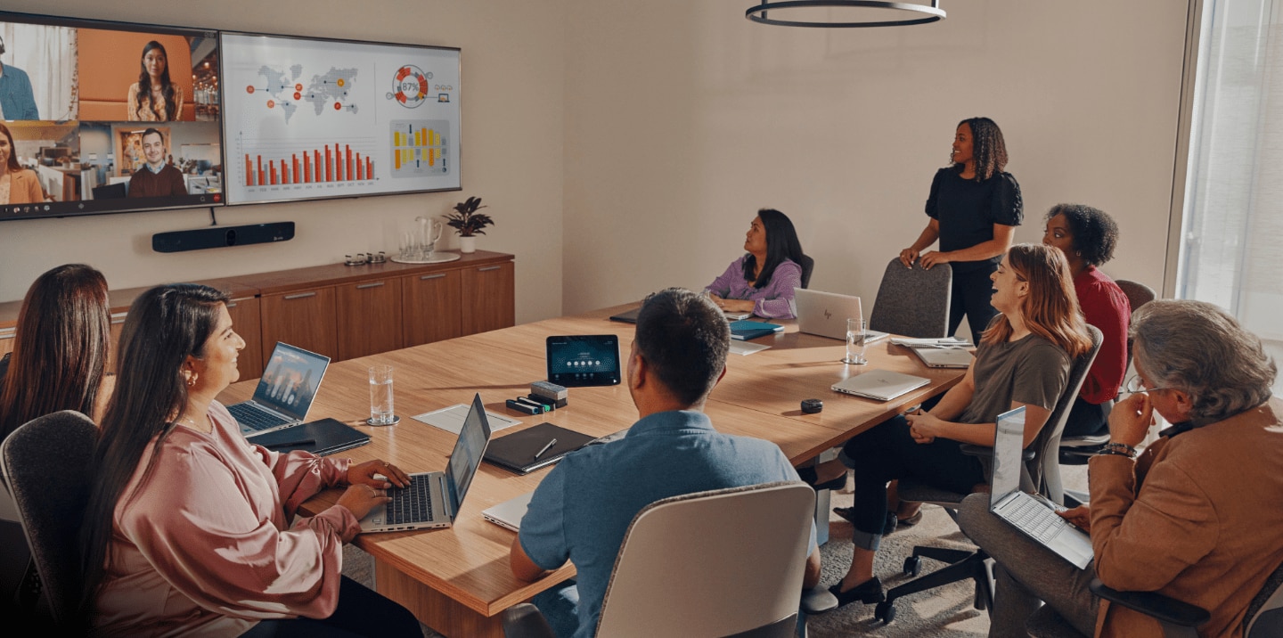  A team meets around a large conference table, with remote colleagues joining from a video feed displayed on an HP wall-mounted monitor.