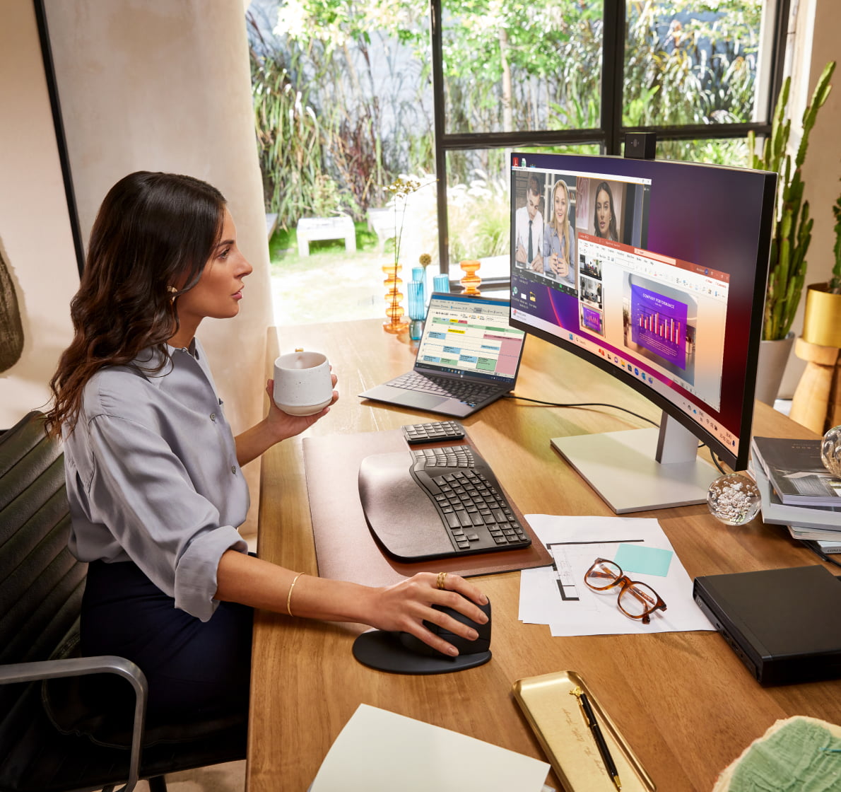 Woman in home office holding coffee mug, using HP mouse while looking at video call on HP curved monitor
