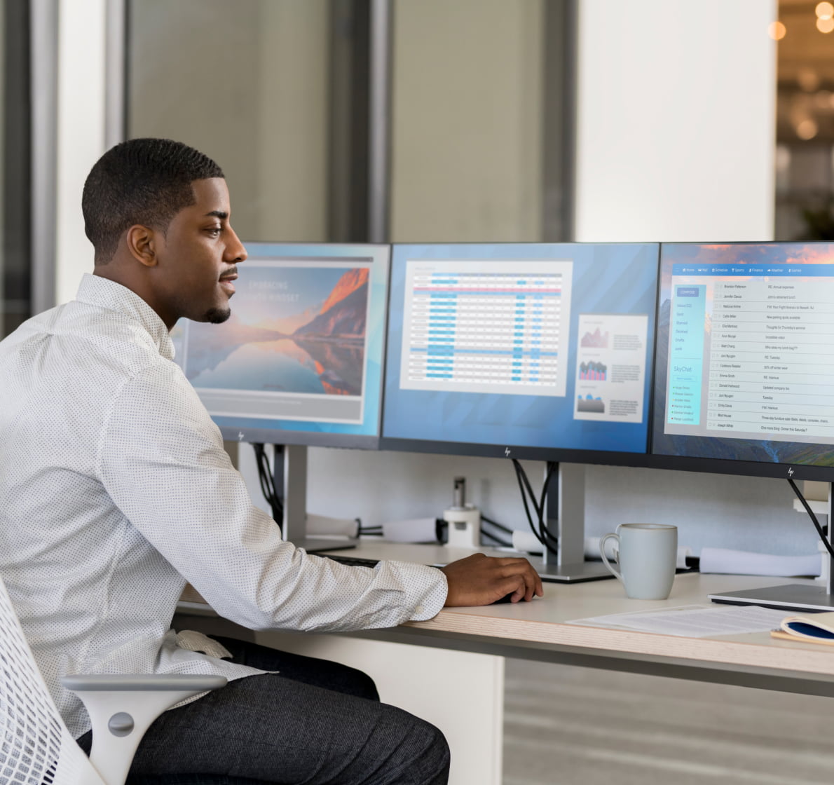 Professional man sitting at office desk looking at three HP monitors