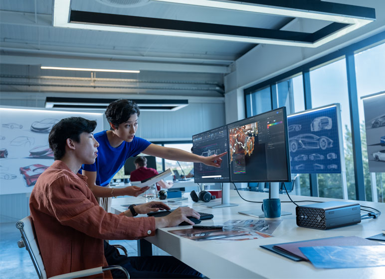 A woman pointing at an HP computer monitor and discussing a project together with her colleague at an office.