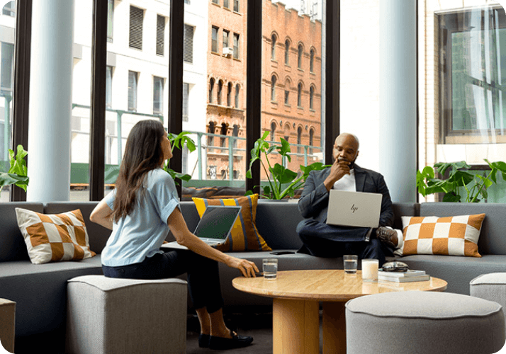 Man and woman with HP laptops in an office, participating in a meeting and sharing ideas.